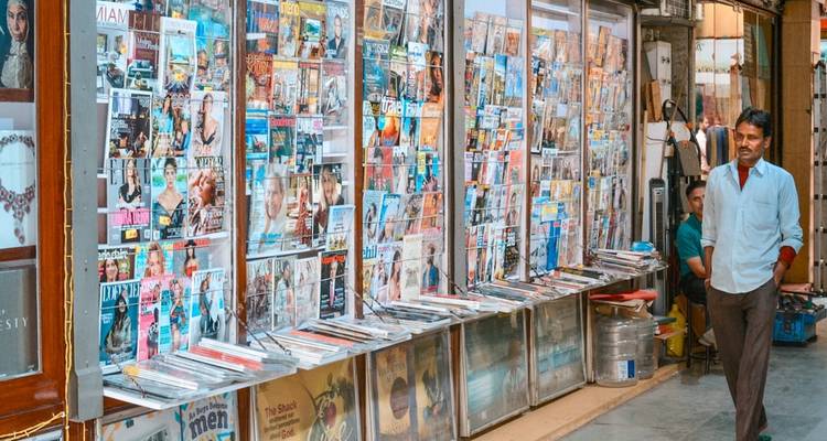 Ein Zeitschriftenstand mit einer Vielzahl bunter Zeitschriften in der Auslage, ein Mann geht vorbei.