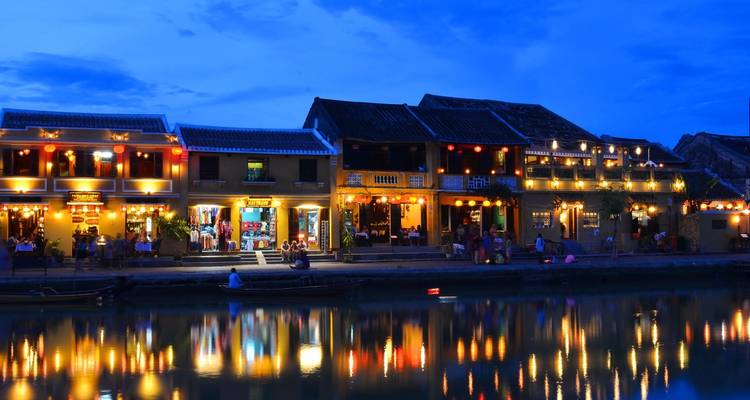 Beleuchtete Gebäude am Flussufer bei Nacht, die sich im Wasser spiegeln.