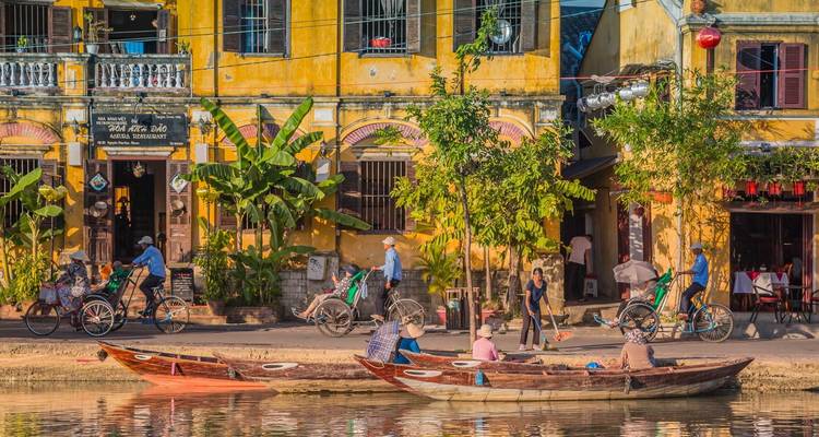 Lebhafte Flussszene mit Booten und gelben Gebäuden.