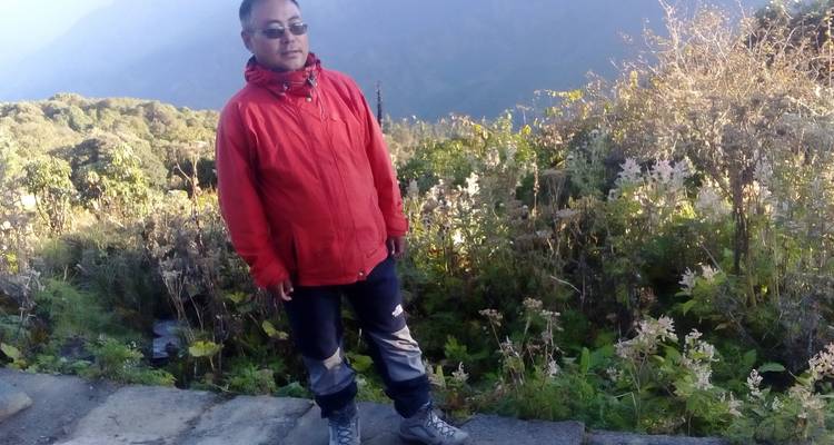 Ein Mann in einer roten Jacke steht auf einem Bergpfad.