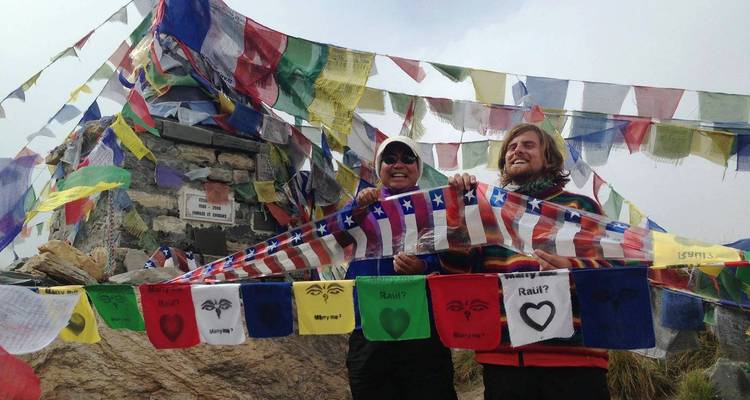 Menschen mit Flaggen und Gebetsfahnen auf einem Berggipfel.