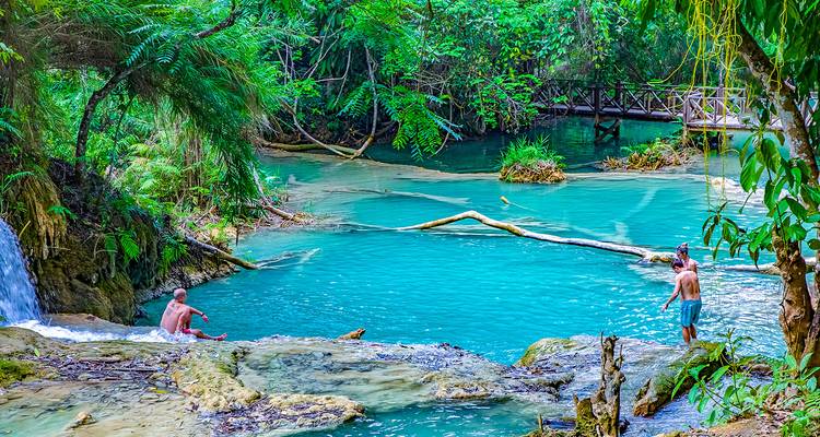 Twee mensen genieten van een natuurlijk watervalbassin omgeven door weelderig groen.