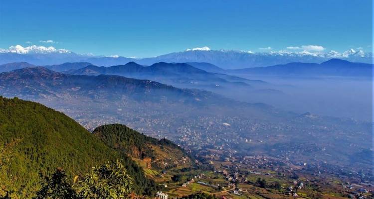 Weite Sicht auf ein Tal mit Bergen, Grün und blauem Himmel.