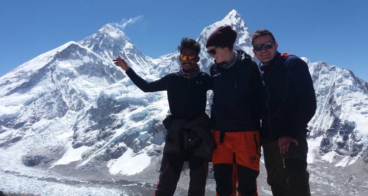 Three people posing with mount Everest and another peak in the background.