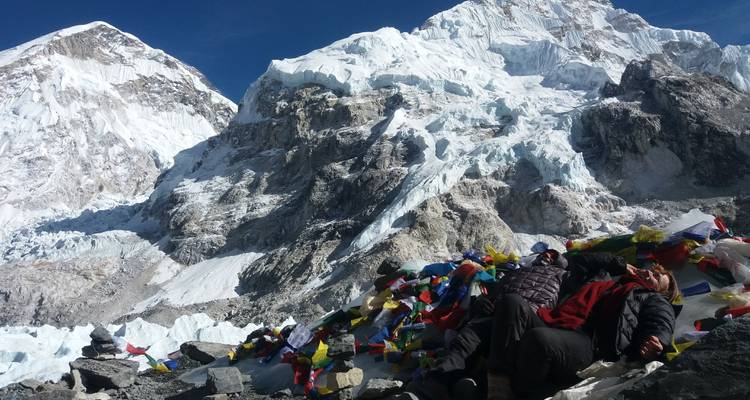 Zwei Menschen ruhen auf Felsen, die mit Gebetsfahnen behangen sind, in den Bergen.