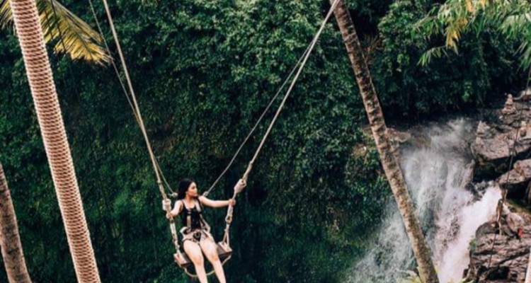 Person auf einer Schaukel mit einem Wasserfall und Wald im Hintergrund.