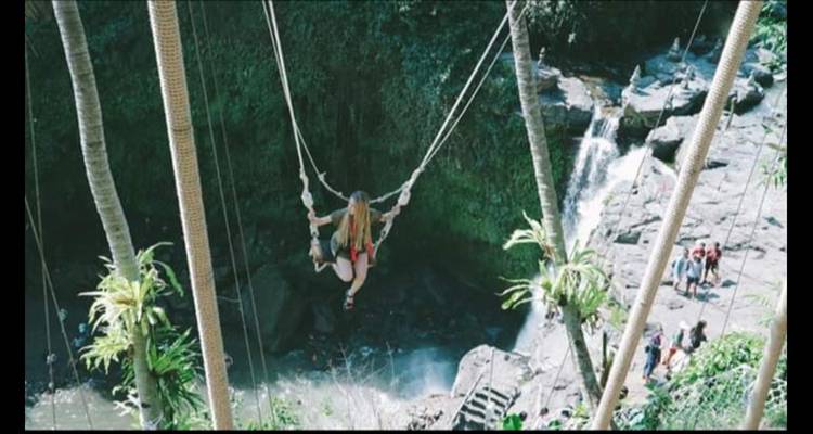 Person auf einer Schaukel über einem Wasserfall, umgeben von üppigem Grün.