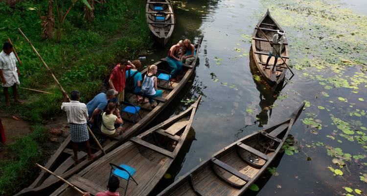 Menschen sitzen in Ruderbooten auf einem ruhigen Gewässer mit Seerosen.