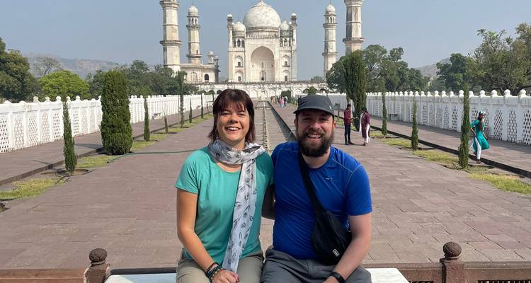 Ein Paar, das vor einem historischen Mausoleum sitzt, das dem Taj Mahal ähnelt.