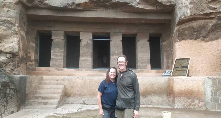 Zwei Touristen stehen vor in Felsen gehauenen Tempelgrotten.