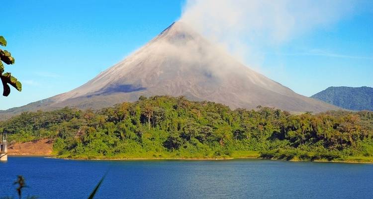 Majestic Arenal Volcano rising above a verdant rainforest with a clear blue sky.