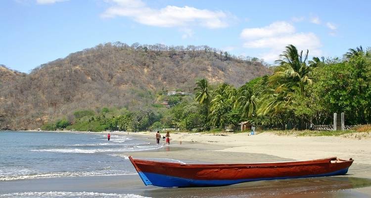 Tropical beach scene with a boat on the shoreline and palm trees in Playa Tamarindo.