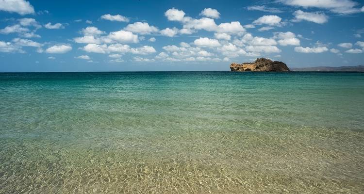 Calm and clear turquoise ocean waters with a rocky island in the distance.