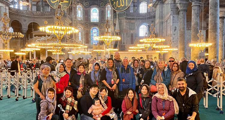 Grand groupe de touristes posant à l'intérieur de l'intérieur orné de Sainte-Sophie avec des lustres lumineux et des mosaïques.