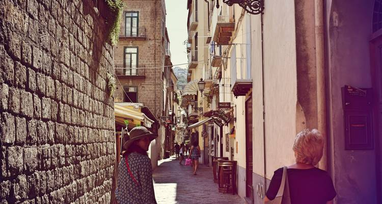 Enge Kopfsteinpflasterstraße mit gehenden Menschen, umgeben von alten Gebäuden in historischer Umgebung.