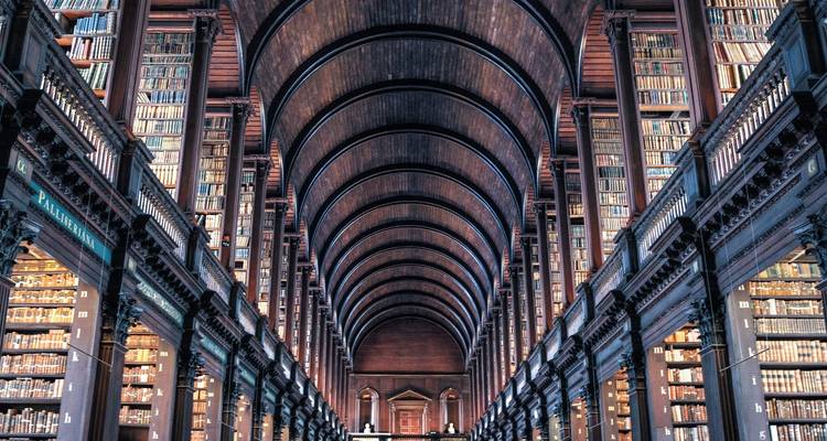 Interior de una biblioteca histórica con altos estantes de madera llenos de libros.