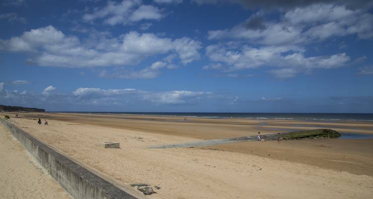Sandstrand mit einigen Besuchern und einem Fernblick auf Klippen.