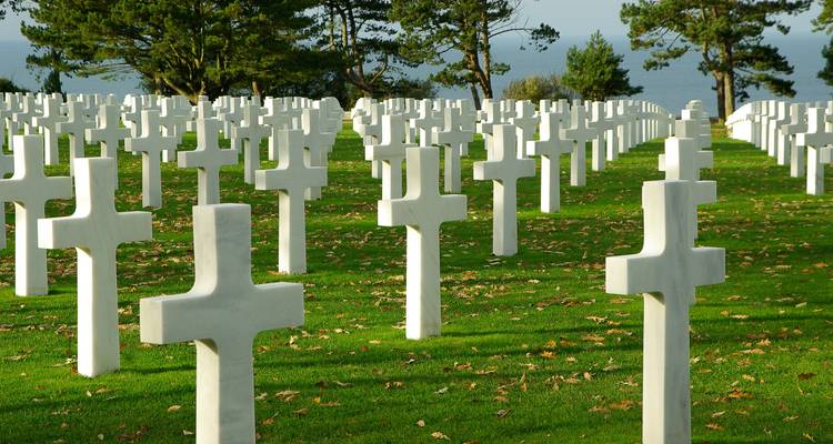Ein Gedenkfriedhof mit Reihen weißer Kreuze und Blick auf das Meer.