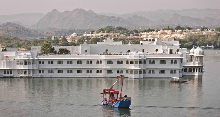 Weißer Palast an einem See mit Bergen im Hintergrund.