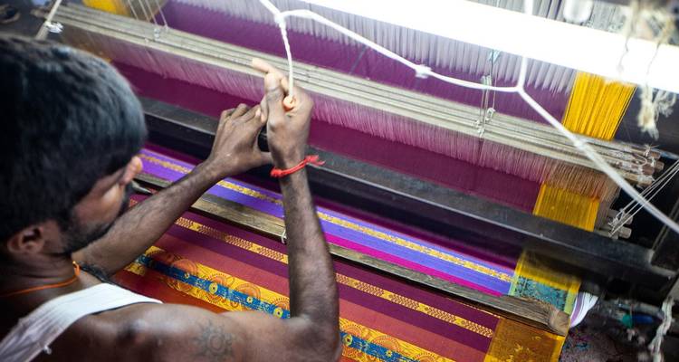 Mann arbeitet an einem traditionellen Webstuhl und webt bunten Stoff.