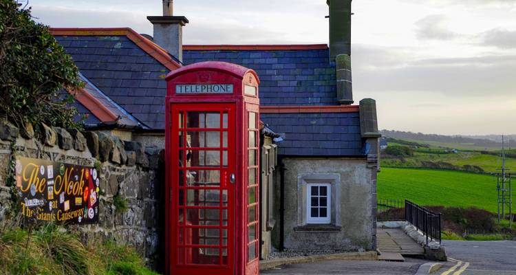 Red telephone box beside traditional buildings with green fields.