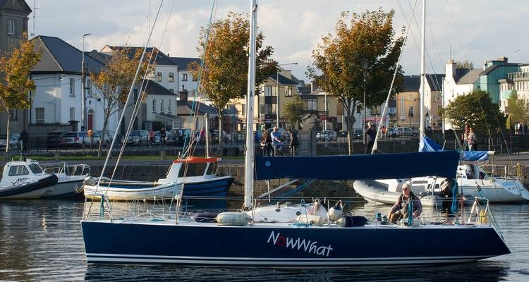 Zeilboot afgemeerd in een haven met een klein stadje op de achtergrond.