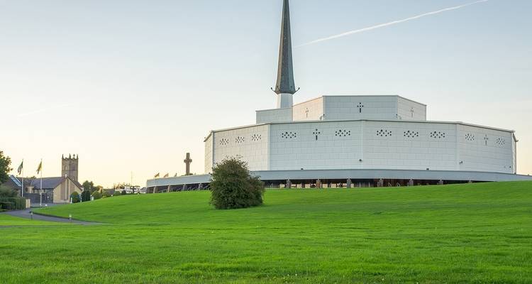 Weißes modernes Kirchengebäude und Kirchturm auf einer Wiese.