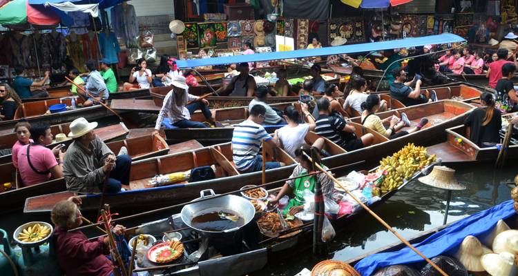 Marché flottant bondé avec des vendeurs cuisinant et vendant des produits à partir de bateaux en bois sur un canal très fréquenté.