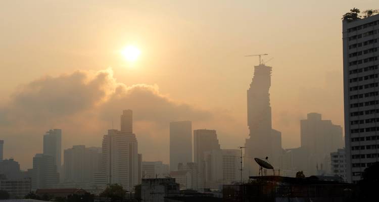 Ligne d'horizon brumeuse de Bangkok se détachant en silhouette contre un lever de soleil orange avec de légers nuages au-dessus de la ville.