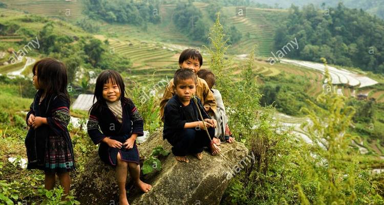 Gruppe lächelnder Kinder auf einem Felsen mit Terrassenfeldern im Hintergrund.