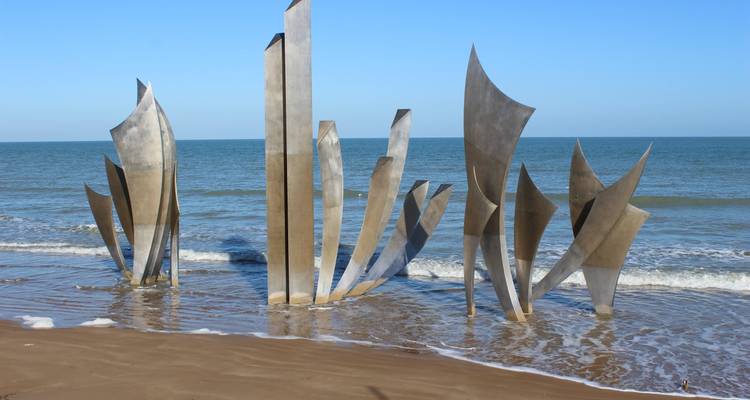 Plage avec sculptures modernes sculptées en forme de vagues dans l'eau peu profonde.