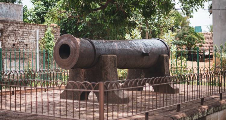 Ancien canon en fer sur des supports en pierre exposé en plein air dans un jardin clôturé.