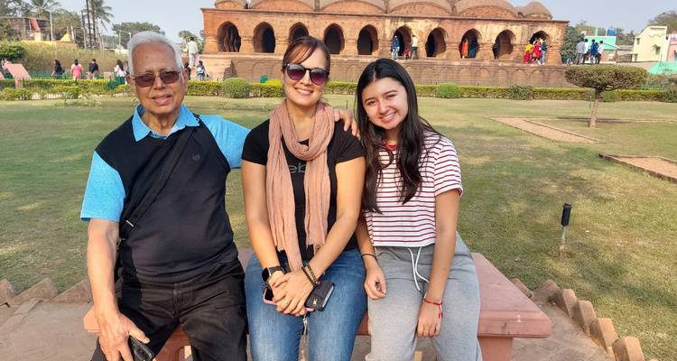 Trois membres d'une famille souriants assis sur un banc avec le temple historique de Rasmancha en arrière-plan.