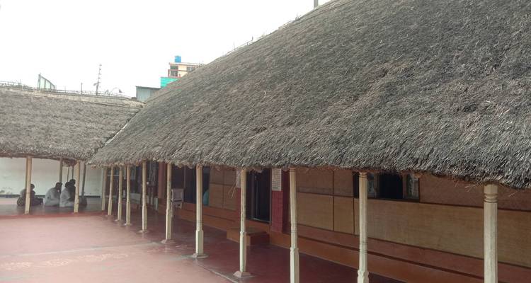 Long véranda au toit de chaume d'un bâtiment traditionnel avec des visiteurs assis à une extrémité.