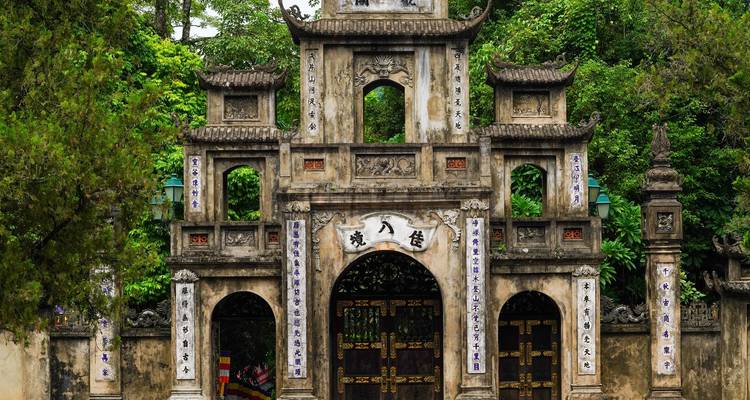 Portón de piedra antiguo y ornamentado de un templo vietnamita rodeado de exuberante vegetación.