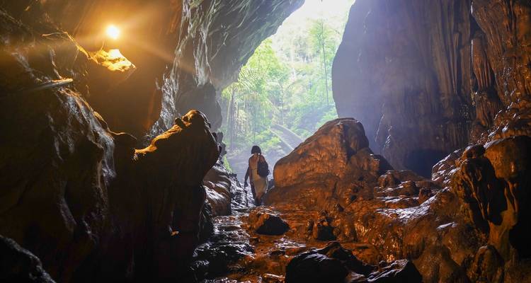 Aventurero con mochila camina por una caverna débilmente iluminada hacia la brillante luz de la selva en la entrada.