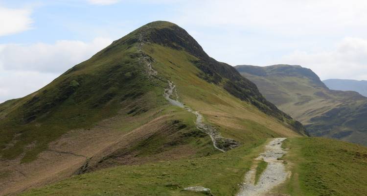 Grasiger Bergpfad, der einen grünen Berg hinaufführt.
