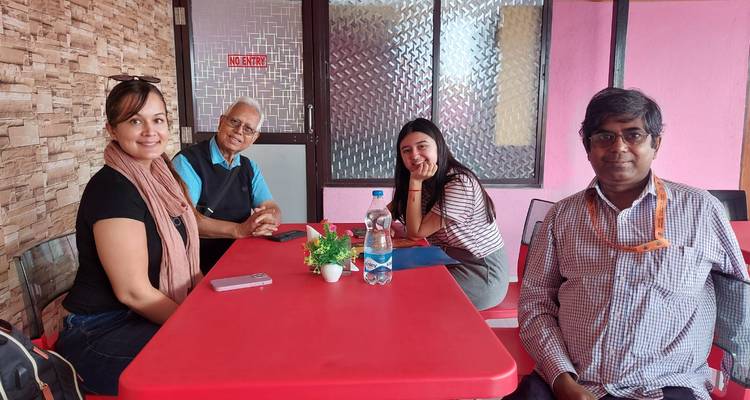Travelers seated around a bright red table inside a simple restaurant posing for camera.