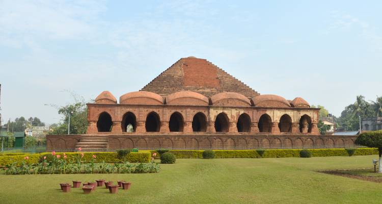 Side view of long brick Rasmancha temple with arches and landscaped lawn.