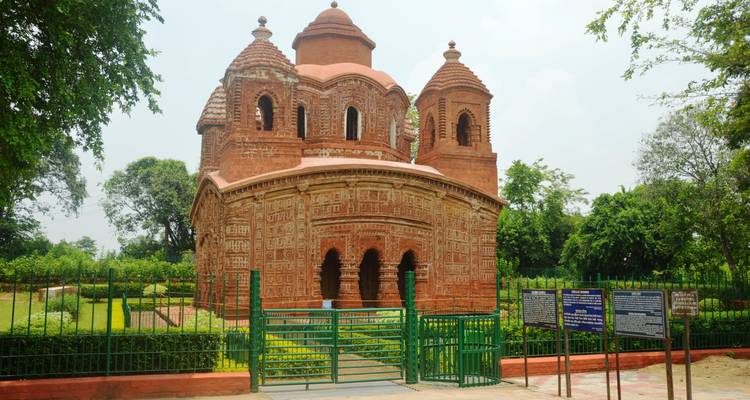 Circular terracotta temple with multiple domes framed by greenery and signboards.