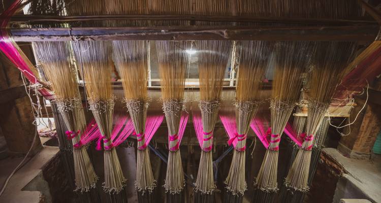 Rows of colorful warp threads hanging in a traditional weaving loom workshop.
