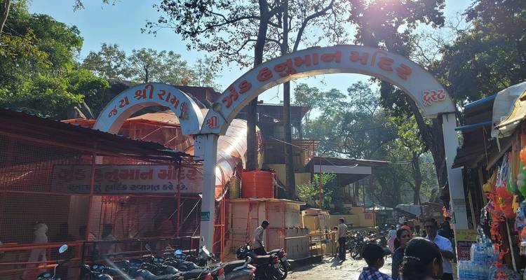 Entrada abarrotada con arco de un complejo de templos hindúes con puestos de mercado y motos afuera.