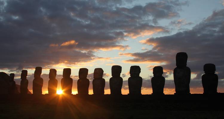 Estatuas Moai silueteadas con un cielo dramático de atardecer.