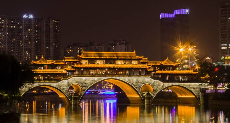 Puente tradicional chino iluminado sobre un río por la noche.