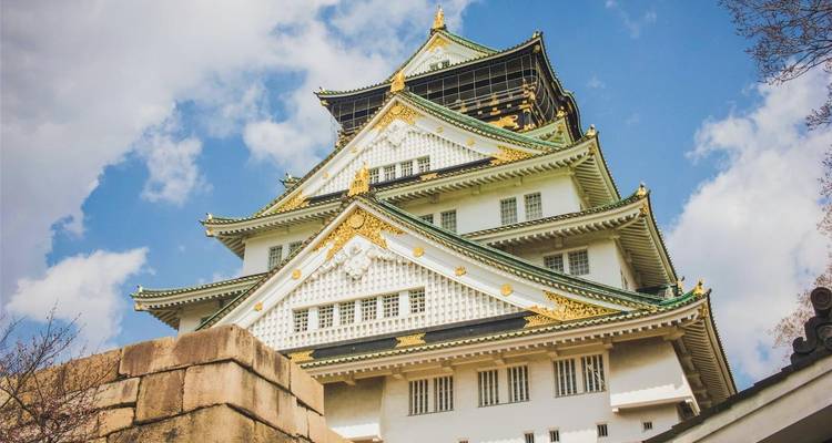 Nahaufnahme der prachtvollen Dachlinien des Osaka-Schlosses, die in heller Sonneneinstrahlung gegen einen wolkigen Himmel glänzen.