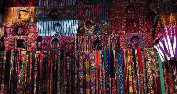 Kleurrijke verscheidenheid aan traditionele kledingstukken en textiel hangend op een markt.