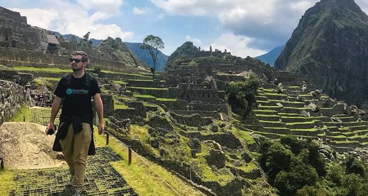 Tourist walking among ancient ruins with mountains in the background.