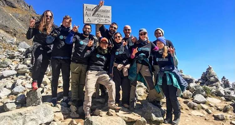 Group of people posing on a rocky path with a sign marking altitude.
