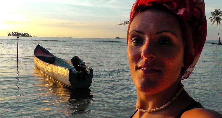Frau bei einem Holzboot und einer Palme bei Sonnenuntergang.