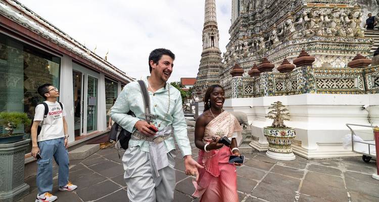 Happy visitors dressed in Thai garments strolling through the intricate Wat Arun complex.